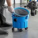 A person using the Lavex Poly Wet / Dry Vacuum to hold a blue bucket with wheels.