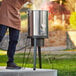 A man pouring water into a large stainless steel pot on a gas stove stand.