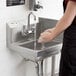 A person washing their hands in a Regency wall mounted hand sink.