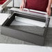 A person using a Vollrath Cubic display kit with a clear roll top cover on a black rectangular box.