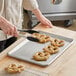 A person cutting a pretzel on a Baker's Mark stainless steel sheet pan.