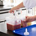 A hand using an Araven condiment pump to pour brown liquid into a plastic container.