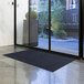 A navy blue Lavex Olefin entrance mat on a floor in front of a glass door.