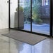 A Lavex Solid Charcoal entrance mat on the floor in front of a glass door.