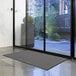 A large gray Lavex Needle Rib indoor entrance mat unrolled in front of a glass door.