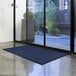 A blue Lavex Waffle entrance mat on the floor in front of a glass door.