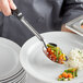 A person holding a Vollrath 3-sided perforated basting spoon over a plate of vegetables.