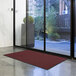 A red Lavex Needle Rib doormat in front of a glass door.