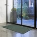 A large green Lavex Needle Rib indoor entrance mat on the floor in front of a glass door.