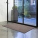 A brown Lavex Olefin entrance mat in front of glass doors.