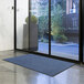 A Lavex blue olefin entrance mat on a floor in front of a glass door.