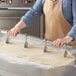 A person in an apron using an Ateco stainless steel pastry cutter to cut dough on a table.