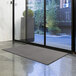 A Lavex Plush solid charcoal entrance mat on the floor in front of a glass door.