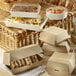 Solia wooden punnet with clear plastic lid filled with sandwiches and fruit on a table.