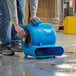 A man using a Lavex blue compact air mover to dry a floor.