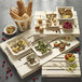 A Solia wooden tray on a table with bread, vegetables, and olives.