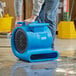 A man using a Lavex blue commercial air mover to clean the floor in a grocery store aisle.