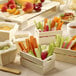 A group of small Solia mini wooden crates with vegetables in them on a table with different foods.