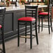A Lancaster Table & Seating black wood bar stool with a red vinyl seat.