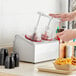 A person pouring red liquid into a Steril-Sil stainless steel condiment dispenser.