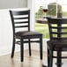 A Lancaster Table & Seating black wood ladder back chair with dark brown vinyl seat on a table in a restaurant.