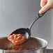 A person holding a Linden Sweden black high-heat nylon prep spoon full of food over a bowl.