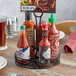 A black wrought iron condiment caddy with leaf design holding hot sauce bottles on a table.