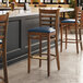 A Lancaster Table & Seating wood ladder back bar stool with a navy vinyl seat at a table in a bar.