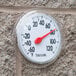 A Taylor 6" dial thermometer on a brick wall.
