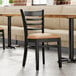 A Lancaster Table & Seating wood ladder back chair with a light brown vinyl seat next to a table in a restaurant dining area.