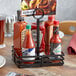 An American Metalcraft wrought iron rectangular condiment caddy holding hot sauce bottles on a table.
