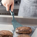 A person using a Linden Sweden Gourmaid gray silicone spatula to cook burgers on a grill.