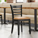 A Lancaster Table & Seating wood ladder back chair with a light brown vinyl seat detached from a table.