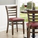 Two Lancaster Table & Seating wood ladder back chairs with burgundy vinyl seats at a table in a restaurant