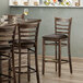 A Lancaster Table & Seating wood ladder back bar stool with dark brown vinyl seat at a table in a restaurant.