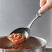 A person using a Linden Sweden Gourmaid high-heat nylon prep spoon to pour food into a pot.