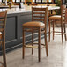 A Lancaster Table & Seating wooden bar stool with a light brown vinyl seat.