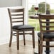 Two Lancaster Table & Seating wood ladder back chairs with black vinyl seats on a restaurant dining area table.