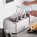 A person using a Steril-Sil stainless steel condiment dispenser to pour liquid into a cup.