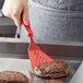 A person using a Linden Sweden red silicone spatula to cook burgers on a pan.