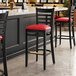 A Lancaster Table & Seating black wood bar stool with red vinyl seat.