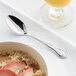 An Acopa stainless steel teaspoon next to a bowl of oatmeal with fruit slices.