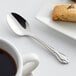 An Acopa stainless steel demitasse spoon on a plate next to a cup of coffee.