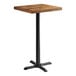 A Lancaster Table & Seating square wooden table with a black metal base.