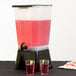 A Tablecraft black beverage dispenser with two glasses of pink liquid and lime slices.