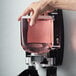 A hand holding a GOJO Cranberry liquid soap dispenser filled with pink liquid.