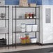 A black epoxy four-shelf storage rack with various food containers and kitchen supplies placed on the shelves.