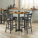 A Lancaster Table & Seating wood butcher block bar height table with black chairs and a wood table.