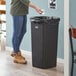 A woman standing next to a Lavex black square trash can.