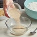 A person pouring red powder into a bowl.